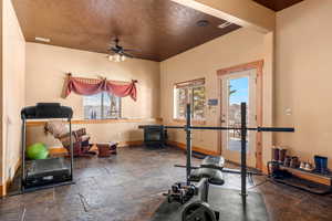 Exercise room featuring plenty of natural light, a ceiling fan, stone tile floors, and a wood stove