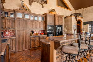 Kitchen featuring dark countertops, a breakfast bar, brown cabinets, black appliances, and high vaulted ceiling