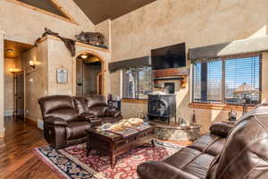 Living area featuring a wood stove, hardwood / wood-style floors, high vaulted ceiling, healthy amount of natural light, and a textured wall