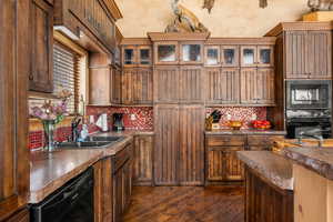 Kitchen with black appliances, glass insert cabinets, dark countertops, dark wood-type flooring, and brown cabinetry