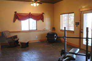 Workout area with plenty of natural light, ceiling fan, and dark stone finish floors