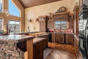 Kitchen featuring glass insert cabinets, a textured wall, dark wood-style flooring, black appliances, and a high ceiling