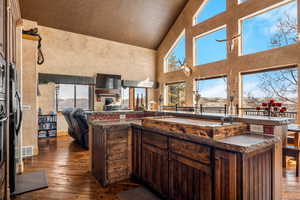 Kitchen featuring dark brown cabinets, a kitchen island with sink, dark wood-style flooring, high vaulted ceiling, and open floor plan