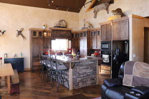 Kitchen featuring a kitchen breakfast bar, black appliances, a center island with sink, glass insert cabinets, and a towering ceiling
