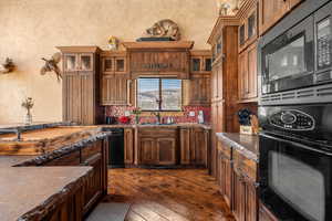 Kitchen featuring black appliances, glass insert cabinets, dark stone counters, and dark wood-type flooring