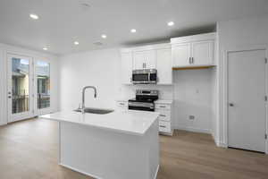 Kitchen featuring white cabinets, stainless steel appliances, a kitchen island with sink, light stone countertops, and light wood-style floors