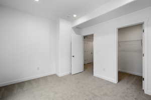 Unfurnished bedroom featuring light carpet, a walk in closet, and recessed lighting