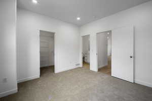 Unfurnished bedroom with light carpet, a spacious closet, recessed lighting, and ensuite bath