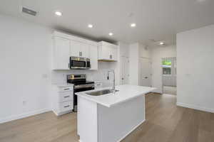 Kitchen featuring appliances with stainless steel finishes, decorative backsplash, white cabinets, a center island with sink, and light wood-type flooring