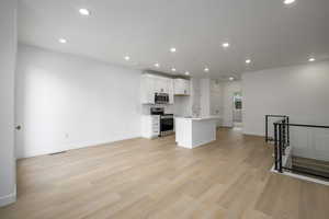 Kitchen featuring stainless steel appliances, an island with sink, white cabinetry, recessed lighting, and light wood-style flooring