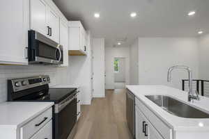Kitchen featuring appliances with stainless steel finishes, white cabinets, light wood finished floors, tasteful backsplash, and recessed lighting