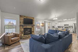 Living room featuring wood finished floors, a chandelier, and a stone fireplace