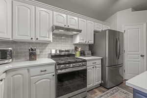 Kitchen featuring appliances with stainless steel finishes, decorative backsplash, under cabinet range hood, dark wood-type flooring, and light stone counters