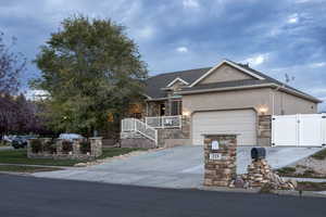 Single story home with stone siding, concrete driveway, stucco siding, a gate, and a porch