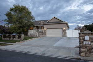 Ranch-style home with a gate, stone siding, concrete driveway, stucco siding, and covered porch