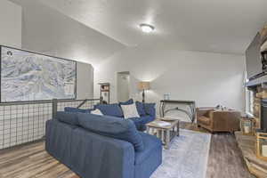 Living area with vaulted ceiling, dark wood-type flooring, a stone fireplace, and a textured ceiling
