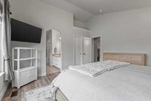 Bedroom featuring vaulted ceiling, arched walkways, light wood-style floors, and ensuite bathroom
