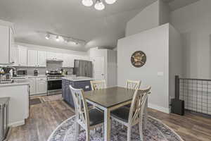 Dining area with dark wood-type flooring, a chandelier, rail lighting, and lofted ceiling