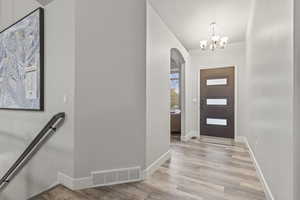 Entrance foyer featuring light wood-style floors, arched walkways, and a chandelier