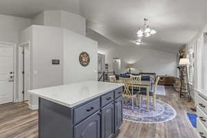 Kitchen featuring lofted ceiling, a kitchen island, dark wood-style flooring, open floor plan, and light stone countertops