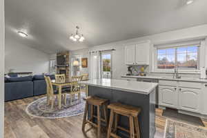 Kitchen with a breakfast bar area, white cabinets, open floor plan, light wood-style floors, and vaulted ceiling