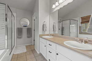Full bathroom with double vanity, a stall shower, light tile patterned floors, a bathtub, and lofted ceiling