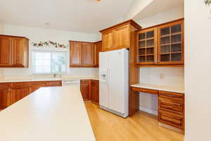 Kitchen featuring brown cabinets, white appliances, built in desk, light countertops, and light wood finished floors