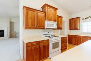 Kitchen featuring white appliances, light countertops, brown cabinetry, a tiled fireplace, and lofted ceiling