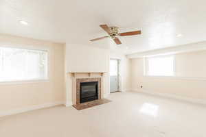 Unfurnished living room featuring a tiled fireplace, carpet, recessed lighting, a textured ceiling, and a ceiling fan