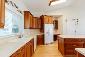 Kitchen with white appliances, brown cabinets, light countertops, light wood-style floors, and lofted ceiling
