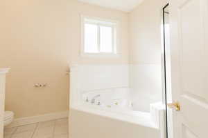 Bathroom with a jetted tub, tile patterned flooring, and a shower with door