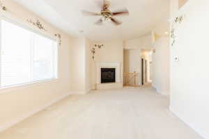 Unfurnished living room featuring light carpet, a fireplace, ceiling fan, and vaulted ceiling