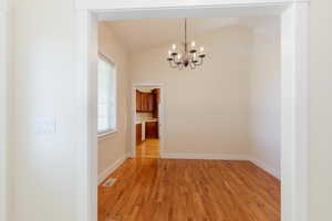 Unfurnished dining area with light wood-type flooring, vaulted ceiling, and a chandelier