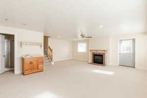 Unfurnished living room with a tiled fireplace, light colored carpet, stairs, ceiling fan, and a textured ceiling