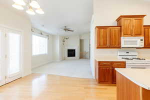 Kitchen featuring white appliances, brown cabinetry, light countertops, a chandelier, and open floor plan