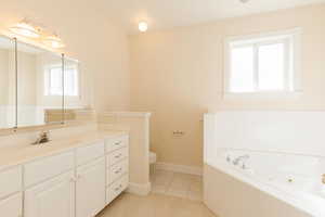 Full bathroom featuring a tub with jets, vanity, healthy amount of natural light, and light tile patterned floors