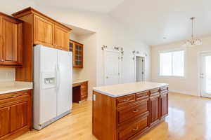Kitchen with brown cabinets, white refrigerator with ice dispenser, a center island, light wood finished floors, and lofted ceiling