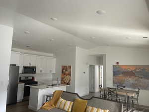 Kitchen with stainless steel appliances, white cabinetry, light countertops, dark wood finished floors, and lofted ceiling