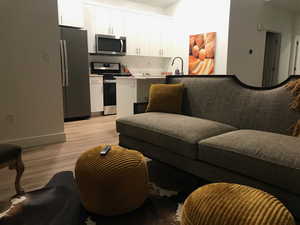 Kitchen featuring appliances with stainless steel finishes, white cabinets, light wood-style flooring, light countertops, and open floor plan