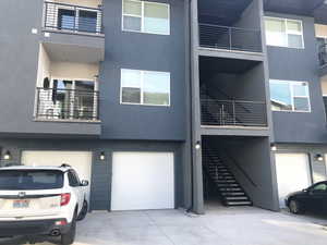 View of front facade featuring stucco siding, a balcony, an attached garage, and driveway