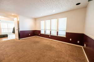 Unfurnished room featuring a textured ceiling, recessed lighting, carpet, and a wainscoted wall