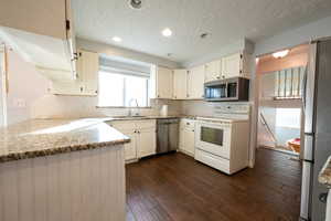 Kitchen featuring stainless steel appliances, light stone countertops, a textured ceiling, dark wood finished floors, and recessed lighting