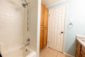 Bathroom with vanity, tub / shower combination, light tile patterned floors, and a textured ceiling