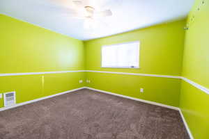 Unfurnished room featuring dark colored carpet and a ceiling fan