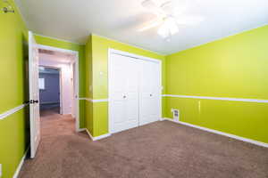 Unfurnished bedroom with dark colored carpet, a closet, a ceiling fan, and a textured ceiling