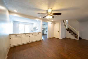 Kitchen with dark wood-style floors, white cabinets, a textured ceiling, ceiling fan, and light stone countertops