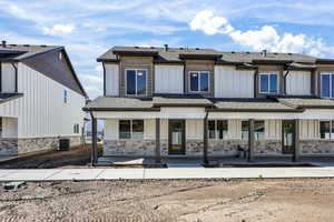 Rear view of property featuring roof with shingles, board and batten siding, a porch, and stone siding