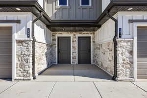 Entrance to property featuring stone siding, a garage, board and batten siding, and a porch