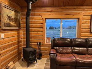 Tiled living area featuring a wood stove, log walls, and wooden ceiling