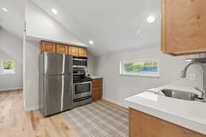 Kitchen with stainless steel appliances, brown cabinetry, recessed lighting, vaulted ceiling, and light wood-style floors